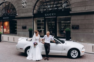Güzel genç bir çift gelin ve damat şehirde beyaz düğün arabasının yanında poz veriyorlar.