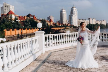 Şehirde poz veren zarif beyaz gelinlik içindeki güzel genç gelinin portresi.          