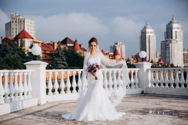 Şehirde poz veren zarif beyaz gelinlik içindeki güzel genç gelinin portresi.          