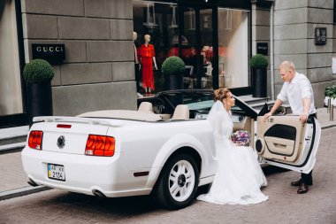 Güzel genç bir çift gelin ve damat şehirde beyaz düğün arabasının yanında poz veriyorlar.