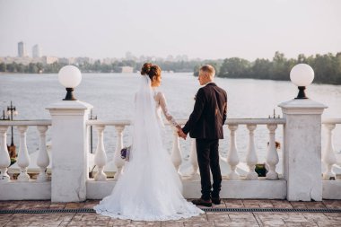 Güzel, genç, mutlu gelin ve damat düğün günü nehir kenarında poz veriyor.               