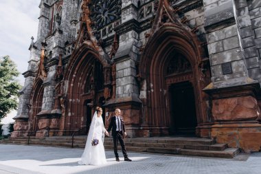 Güzel genç gelin ve damat eski kilisenin önünde yürüyor.        