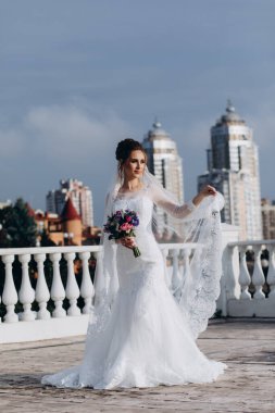Şehirde poz veren zarif beyaz gelinlik içindeki güzel genç gelinin portresi.          