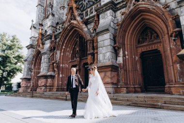 Güzel genç gelin ve damat eski kilisenin önünde yürüyor.        