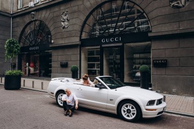 Güzel genç bir çift gelin ve damat şehirde beyaz düğün arabasının yanında poz veriyorlar.