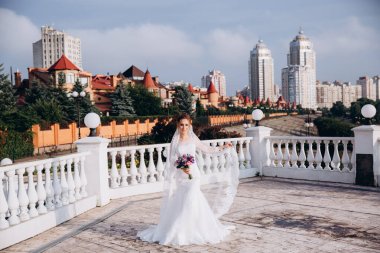 Şehirde poz veren zarif beyaz gelinlik içindeki güzel genç gelinin portresi.          