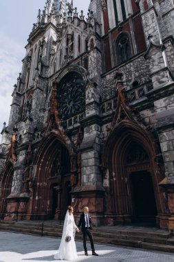 Güzel genç gelin ve damat eski kilisenin önünde yürüyor.        