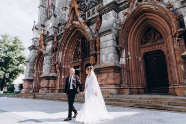 Güzel genç gelin ve damat eski kilisenin önünde yürüyor.        