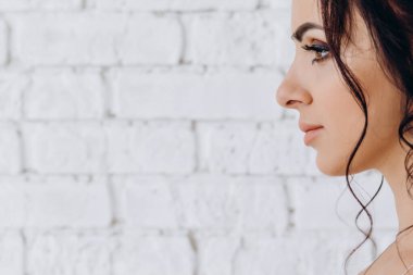 Beyaz tuğladan duvar arkasında güzel esmer gelinin yan görüntüsü 