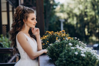 Gelinlik giymiş, terasta dikilmiş, yana bakan düşünceli genç gelinin yan görünüşü