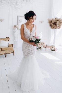 Beyaz elbiseli güzel genç gelin zarif iç kısımda düğün buketi ile poz veriyor.          