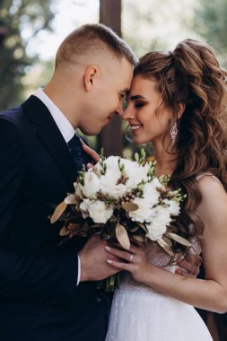 Genç bir çift düğün günlerinde güneşli bir yaz parkında romantik bir anın tadını çıkarır. Doğayla çevrili, gülümsüyor ve birbirlerine sevgiyle sarılıyorlar..