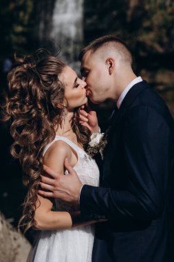 Genç bir çift düğün günlerinde güneşli bir yaz parkında romantik bir anın tadını çıkarır. Doğayla çevrili, gülümsüyor ve birbirlerine sevgiyle sarılıyorlar..