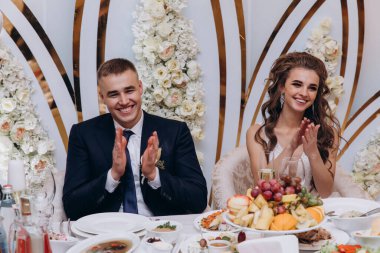 Genç gelin ve damat düğünü kutluyor, masada oturuyor. 