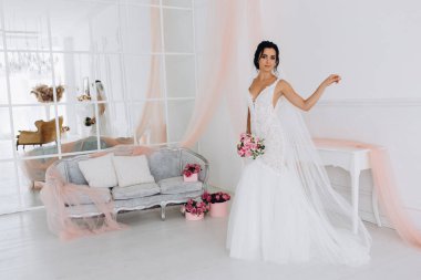 Beyaz elbiseli güzel genç gelin zarif iç kısımda düğün buketi ile poz veriyor.          