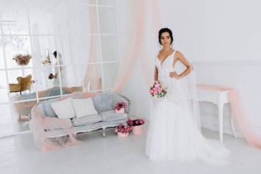 Beyaz elbiseli güzel genç gelin zarif iç kısımda düğün buketi ile poz veriyor.          