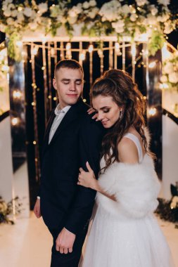 Genç bir düğün çifti, özel günlerinde güzel düğün süslemelerinin önünde romantik bir anın tadını çıkarır..