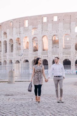 Birbirine aşık çiftler kolezyumun yanında el ele yürüyorlar. 