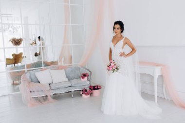 Beyaz elbiseli güzel genç gelin zarif iç kısımda düğün buketi ile poz veriyor.          