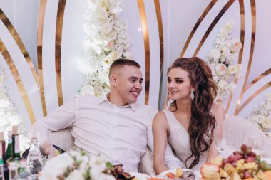 Genç gelin ve damat düğünü kutluyor, masada oturuyor. 