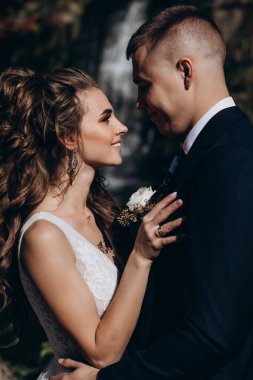 Genç bir çift düğün günlerinde güneşli bir yaz parkında romantik bir anın tadını çıkarır. Doğayla çevrili, gülümsüyor ve birbirlerine sevgiyle sarılıyorlar..