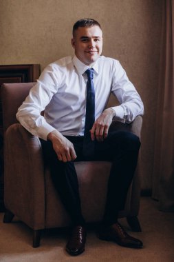 Takım elbiseli yakışıklı bir gencin portresi koltukta oturuyor ve kameraya gülümsüyor.