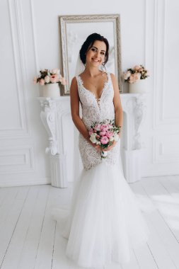 Beyaz elbiseli güzel genç gelin zarif iç kısımda düğün buketi ile poz veriyor.          