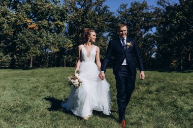 Genç bir çift düğün günlerinde güneşli bir yaz parkında romantik bir anın tadını çıkarır. Doğayla çevrili, gülümsüyor ve birbirlerine sevgiyle sarılıyorlar..