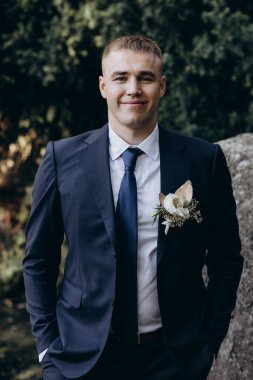 Gelinlik giymiş neşeli genç damat parkta kameraya gülümsüyor.  