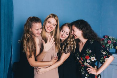 Bir grup mutlu, gülümseyen bayan arkadaş evde bekarlığa veda partisi veriyor. Bir kadın alyansını gösteriyor.