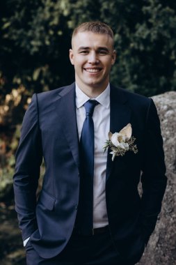 Yakışıklı gülen damat şık bir takım elbise giyip kameraya poz veriyor.