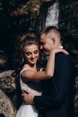 Genç bir çift düğün günlerinde güneşli bir yaz parkında romantik bir anın tadını çıkarır. Doğayla çevrili, gülümsüyor ve birbirlerine sevgiyle sarılıyorlar..