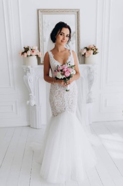 Beyaz elbiseli güzel genç gelin zarif iç kısımda düğün buketi ile poz veriyor.          