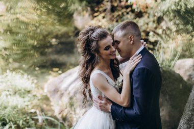 Genç bir çift düğün günlerinde güneşli bir yaz parkında romantik bir anın tadını çıkarır. Doğayla çevrili, gülümsüyor ve birbirlerine sevgiyle sarılıyorlar..