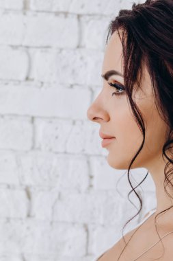 Beyaz tuğladan duvar arkasında güzel esmer gelinin yan görüntüsü 