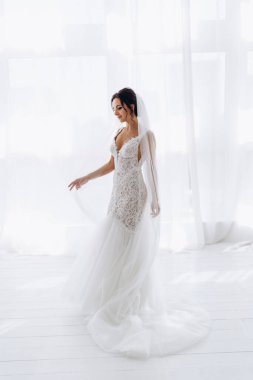 Beyaz gelinlik ve duvak içinde odada poz veren genç gelinin portresi..       