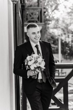 Takım elbiseli yakışıklı genç damat elinde siyah beyaz bir buket tutuyor.