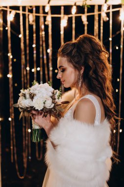 Genç ve güzel bir gelin, özel gününde göz kamaştırıcı düğün süslerinin önünde zarifçe poz verir..