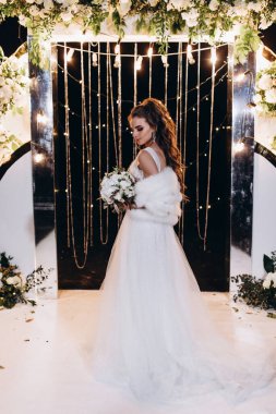 Genç ve güzel bir gelin, özel gününde göz kamaştırıcı düğün süslerinin önünde zarifçe poz verir..