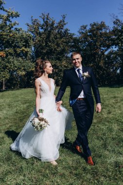 Genç bir çift düğün günlerinde güneşli bir yaz parkında romantik bir anın tadını çıkarır. Doğayla çevrili, gülümsüyor ve birbirlerine sevgiyle sarılıyorlar..