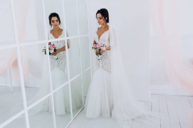 Beyaz elbiseli güzel genç gelin zarif iç kısımda düğün buketi ile poz veriyor.          