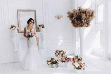 Beyaz elbiseli güzel genç gelin zarif iç kısımda düğün buketi ile poz veriyor.          