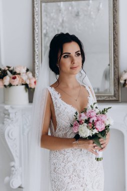 Beyaz elbiseli güzel genç gelin zarif iç kısımda düğün buketi ile poz veriyor.          