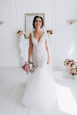 Beyaz elbiseli güzel genç gelin zarif iç kısımda düğün buketi ile poz veriyor.          