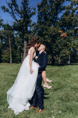 Genç bir çift düğün günlerinde güneşli bir yaz parkında romantik bir anın tadını çıkarır. Doğayla çevrili, gülümsüyor ve birbirlerine sevgiyle sarılıyorlar..