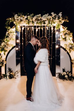 Güzel, mutlu, genç bir çift. Dekoratif çiçek kemerinin yanında dans ediyorlar.          
