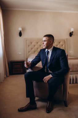 Takım elbiseli genç ve yakışıklı bir adam cam tutuyor ve odada oturuyor. 