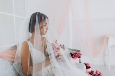 Beyaz gelinlik ve duvak içinde odada poz veren genç gelinin portresi..       