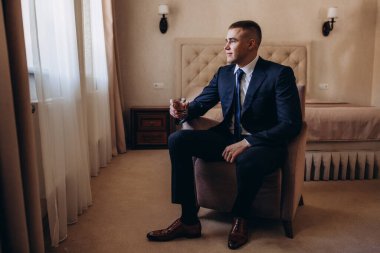 Takım elbiseli genç ve yakışıklı bir adam cam tutuyor ve odada oturuyor. 