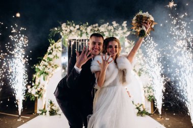 Mutlu gelin ve damat parkta düğün kemerinin yanında poz veriyor.          